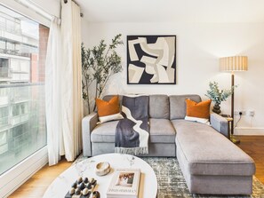 Una sala de estar moderna con un sofá seccional gris, una mesa de centro redonda y un gran ventanal con cortinas.