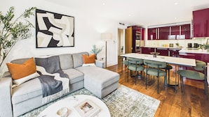 A modern living room with a grey sectional sofa, a coffee table, and a dining area with green chairs. - Westminster Residences by apt. (London)