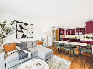A modern living room with a grey sectional sofa, a coffee table, and a dining area with green chairs. - Westminster Residences by apt. (London)