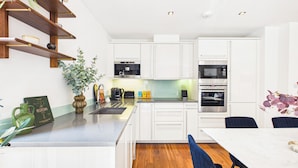 A modern kitchen with white cabinets, a wooden countertop, and a dining area with a table and chairs. - Westminster Residences by apt. (London)