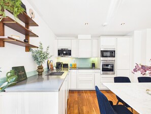 A modern kitchen with white cabinets, a wooden countertop, and a dining area with a table and chairs. - Westminster Residences by apt. (London)