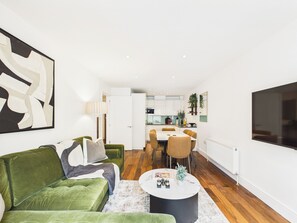 A modern living room with a green sofa, a coffee table, and a dining area with a white table and chairs. - Westminster Residences by apt. (London)