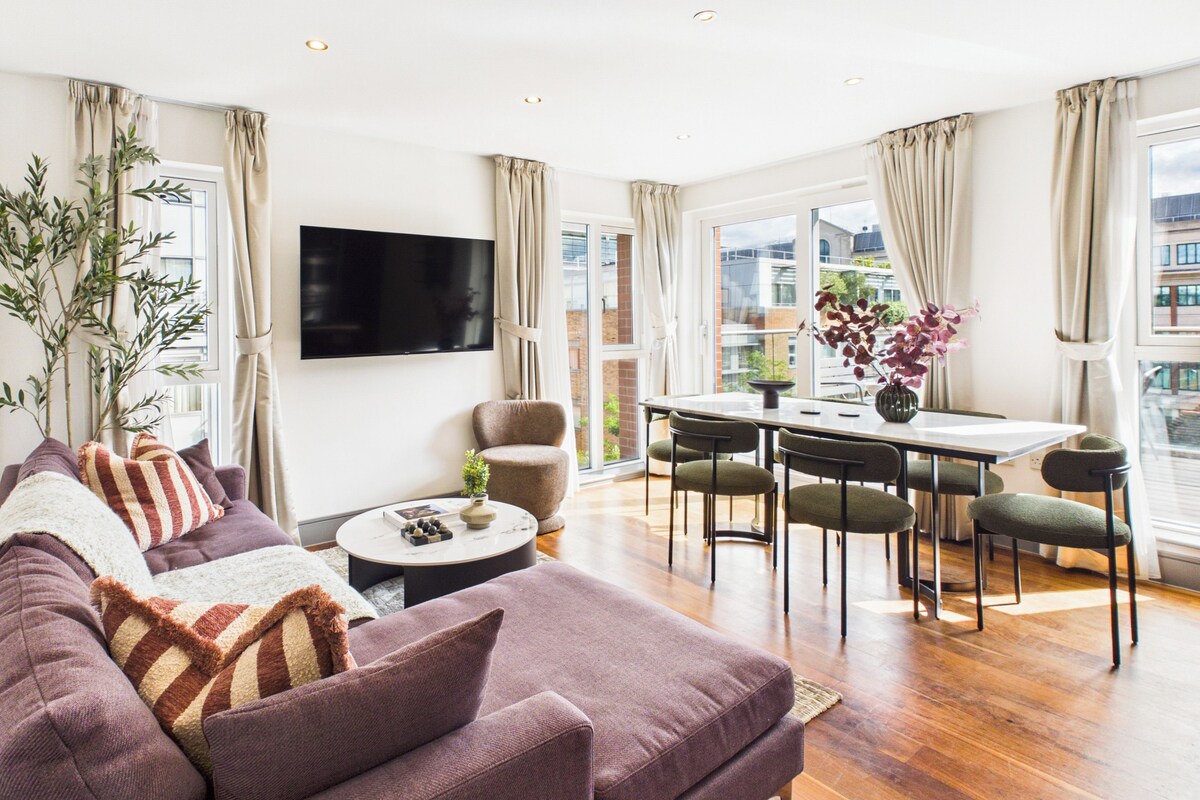 Uma sala de estar moderna com sofá, TV, mesa de jantar, cadeiras e uma janela grande.
