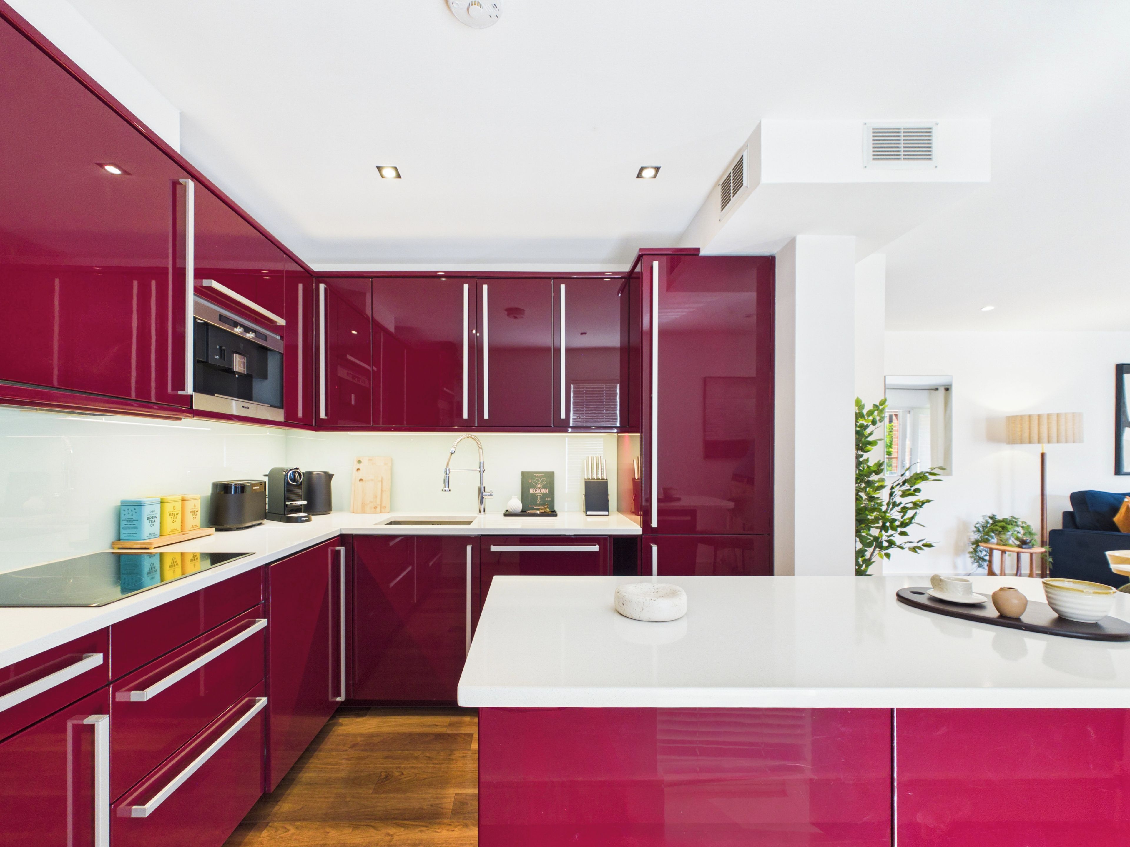 A modern kitchen with red cabinetry, white countertops, and a central island.