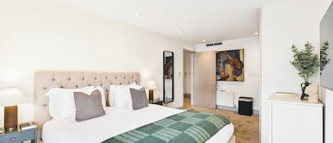 A modern hotel room with a large bed, a bedside table with a lamp, a dresser, and a television on a stand.