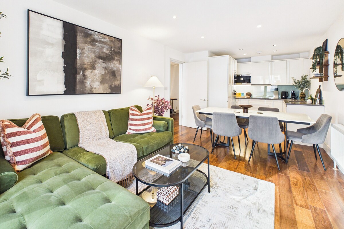 Uma sala de estar moderna com um sofá verde, uma mesa de centro e um espaço de jantar com mesa branca e cadeiras cinzas.