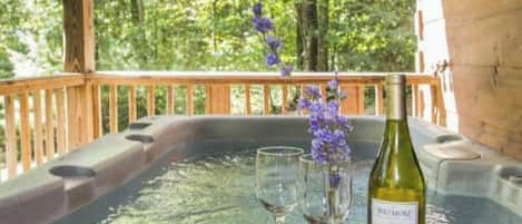 A wooden deck with a hot tub, two wine glasses, a bottle of wine, and purple flowers.