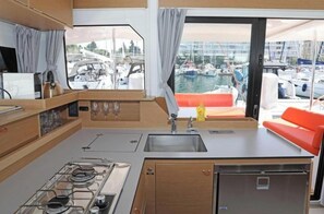 Eine kompakte Küche mit Gasherd, Spüle und Blick auf eine Marina durch ein großes Fenster.