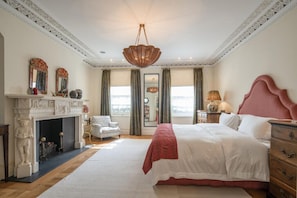Ein Schlafzimmer mit einem großen Bett, einem Kamin, einer Kristallleuchter und Blick auf die Stadt.