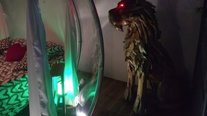 Ett rum med ett runt fönster, en säng med mönstrat sänglinne och en träskulptur.
