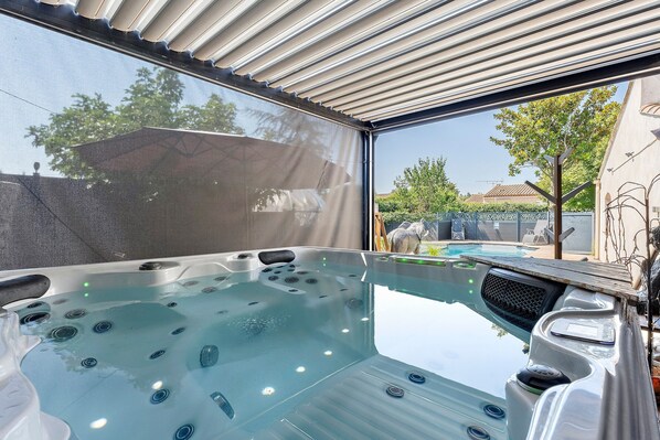 A hot tub with a view of a swimming pool and a house in the background.