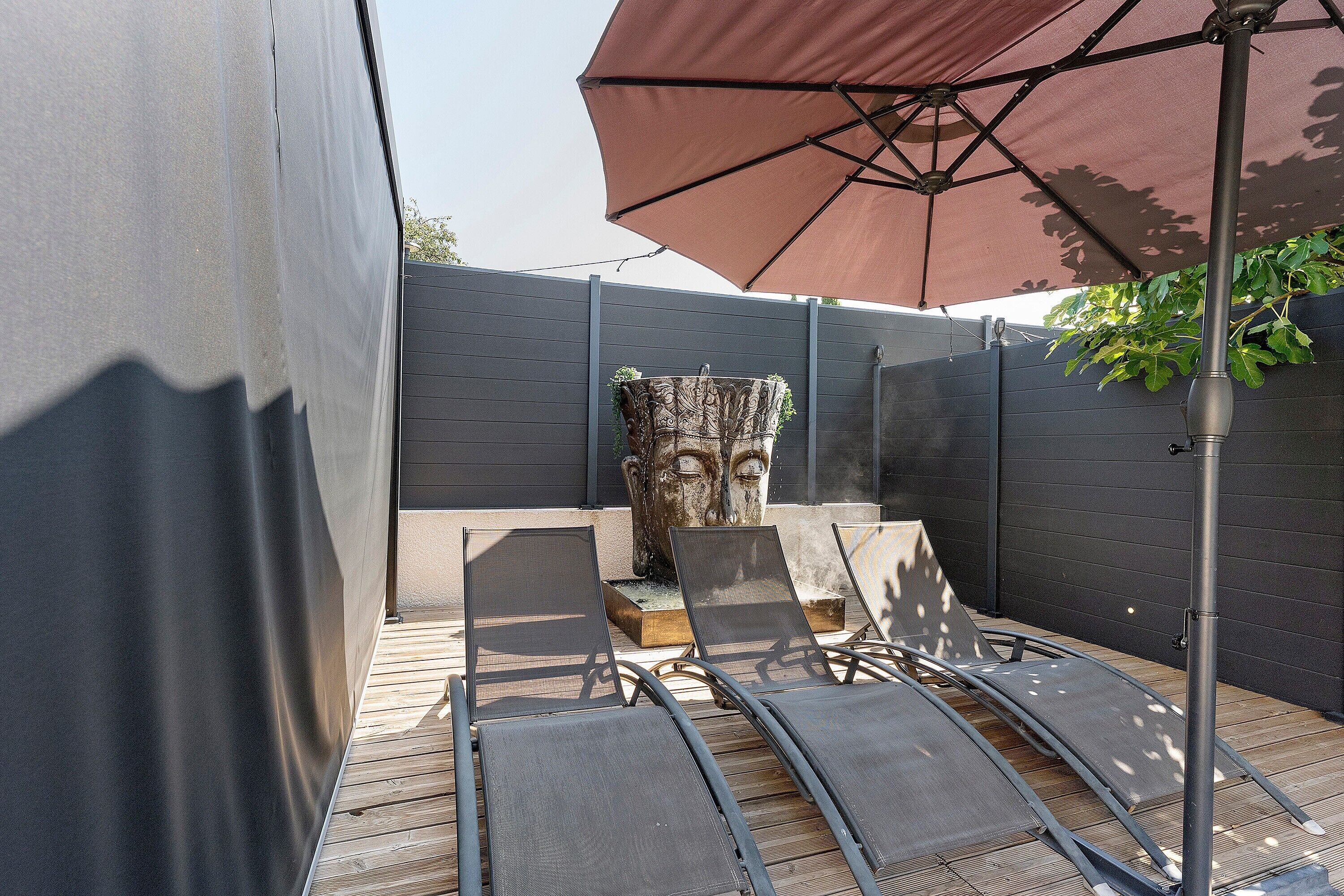 Un'area salotto esterna con una pergola, un muro di pietra decorativo e un ombrellone grande.