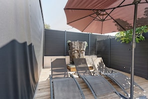 Zona d'estar exterior amb una pérgola, un mur de pedra decoratiu i un parasol gran.