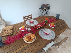 Ein Holztisch mit Frühstücksaufstellung, darunter Croissants, eine Saftflasche und rote Schalen.