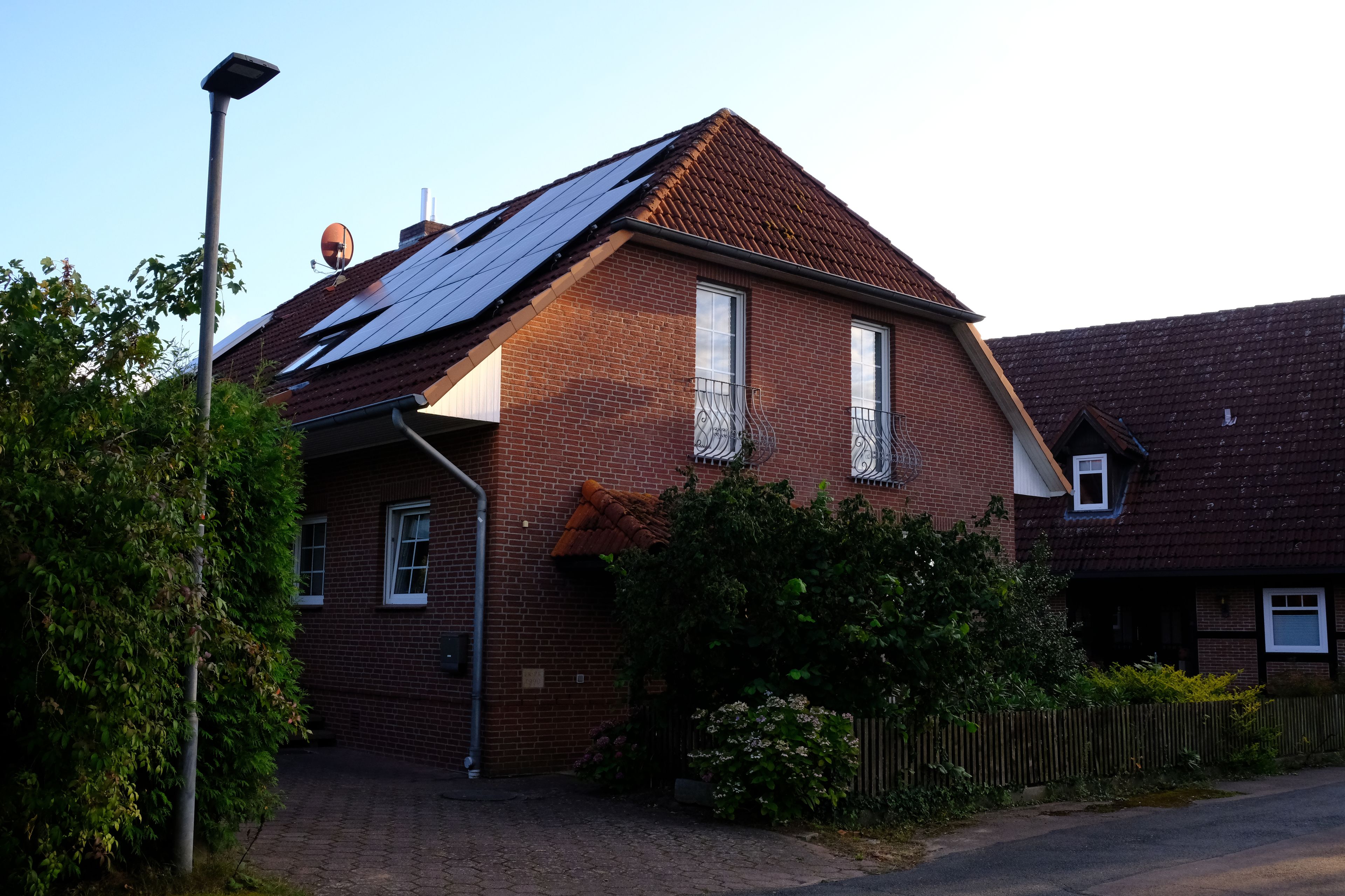 Une maison à deux étages, construite en briques, avec des panneaux solaires sur le toit, une antenne parabolique et une allée pavée.