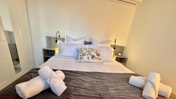 A neatly made bed with white linens and a floral pillow, two white towels, and a bedside table with a lamp and a clock. - Charming 2-room apartment - Ocean view - Pool - Parking - Antibes (Antibes)
