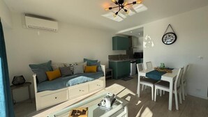 A modern living room with a sofa, dining table, and chairs. There is a kitchen area in the background. - Charming 2-room apartment - Ocean view - Pool - Parking - Antibes (Antibes)