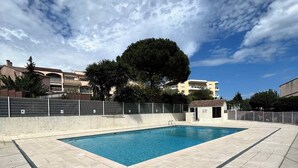 A swimming pool with a tiled deck, surrounded by a fence, under a partly cloudy sky. - Charming 2-room apartment - Ocean view - Pool - Parking - Antibes (Antibes)