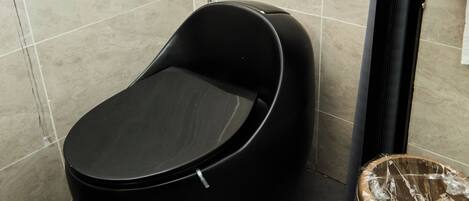 A modern bathroom with a black bathtub, a shower, and a waste basket.