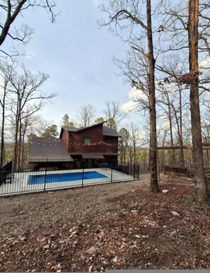 Une cabane avec une piscine, entourée d’arbres et d’une zone délimitée par une clôture.