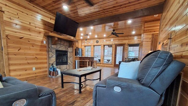 A wooden cabin interior with a stone fireplace, a television mounted on the wall, and a ceiling fan. - Three Bears Pet-friendly Cabin With Heated Pool Near Hochatown Mountain Views Sleeps 10 (Broken Bow)