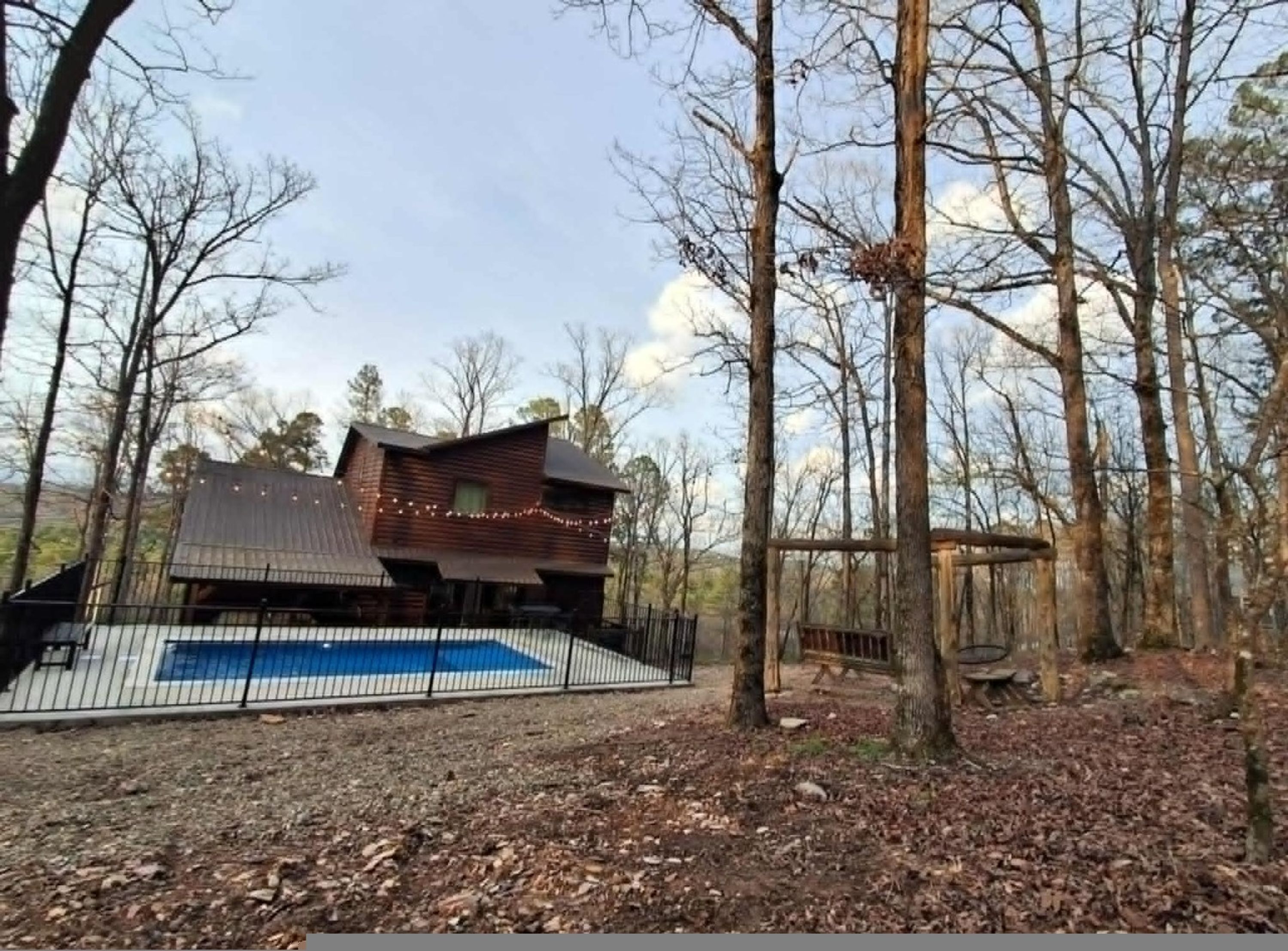 A cabin with a metal roof, surrounded by trees and a fenced area.