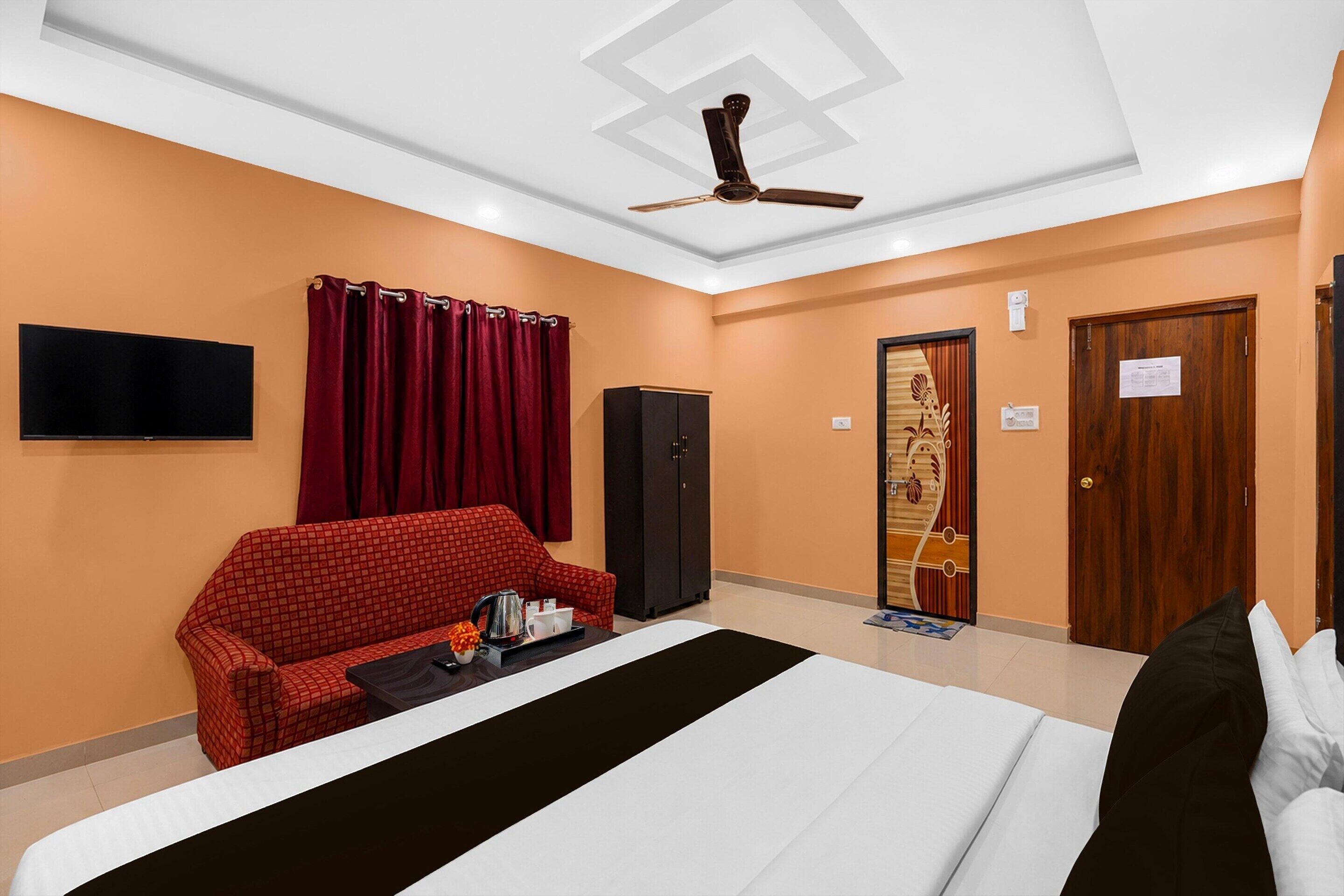 A hotel room with a bed, a red sofa, a flat-screen TV, a ceiling fan, and a wardrobe.