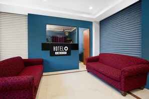 Zona de recepción de un hotel con una pared azul, un mostrador de recepción y dos sofás rojos con estampado.