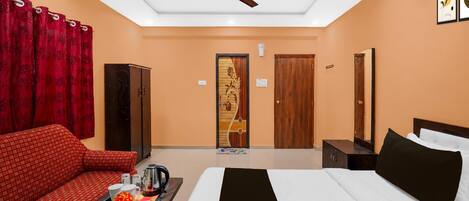 A hotel room with a bed, a sofa, a coffee table, a ceiling fan, and a door with a decorative panel.