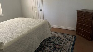 Um quarto com cama, cômoda, porta e tapete estampado.
