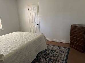 Ein Schlafzimmer mit Bett, Schminktisch, Tür und einem gemusterten Teppich.