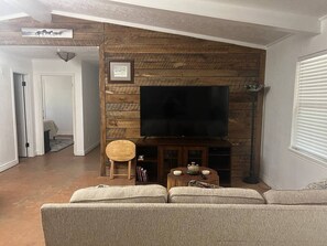 Ein Wohnzimmer mit einem an einer Holzwand montierten Flachbildfernseher, einem runden Holzstuhl, einem kleinen Tisch mit Dekoration und einem Sofa.