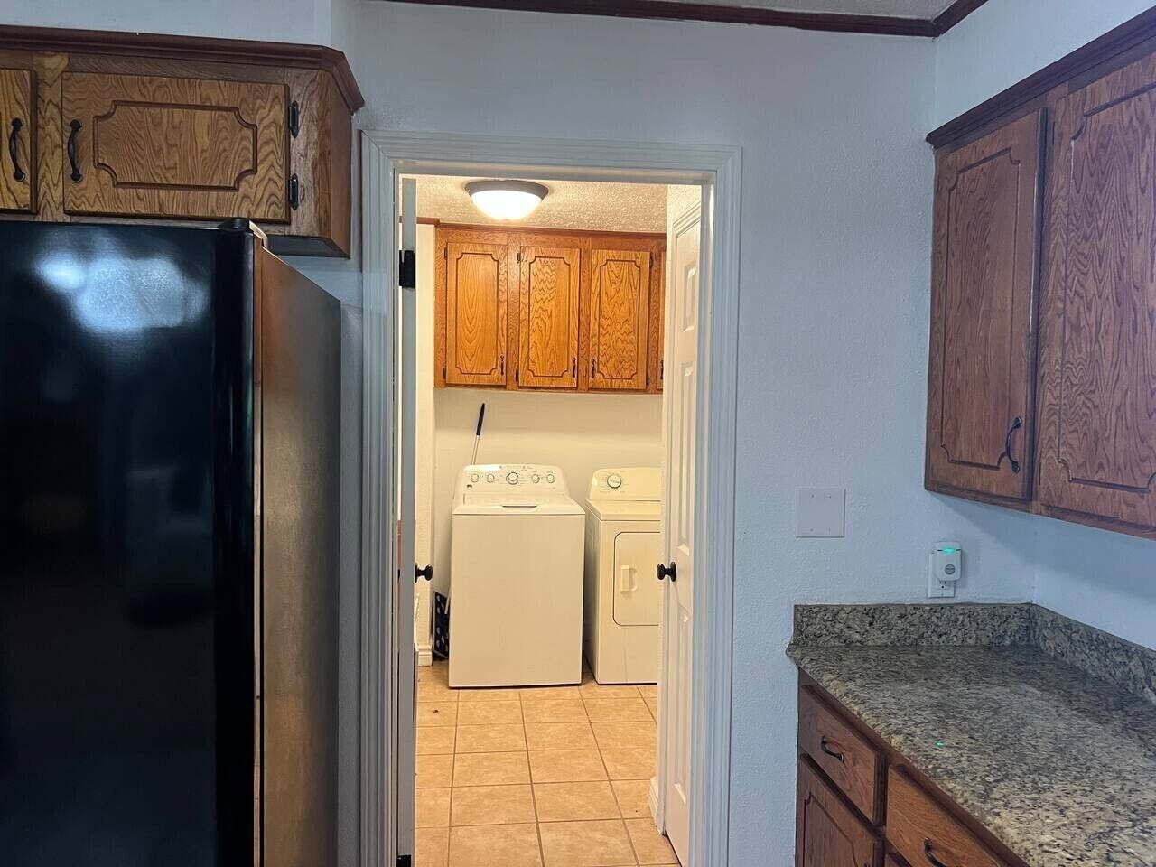 Una cocina con armarios de madera, un refrigerador negro, una lavadora y una encimera de granito.