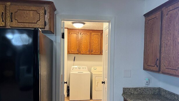 Uma cozinha com armários de madeira, uma geladeira preta, uma máquina de lavar e uma bancada de granito.