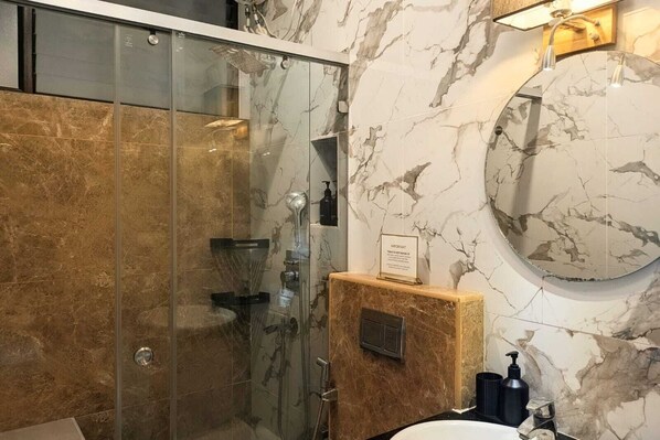 A modern bathroom with a glass-enclosed shower, marble walls, and a wooden vanity with a sink.