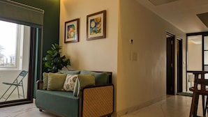 A modern living room with a green sofa, a chair, and two framed artworks on the wall.