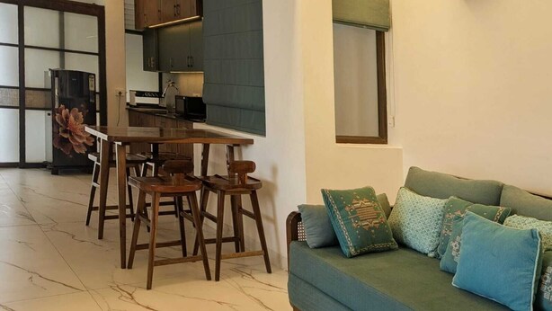 A modern kitchen with dark wooden cabinets, a dining table with bar stools, and a green sofa with patterned cushions.