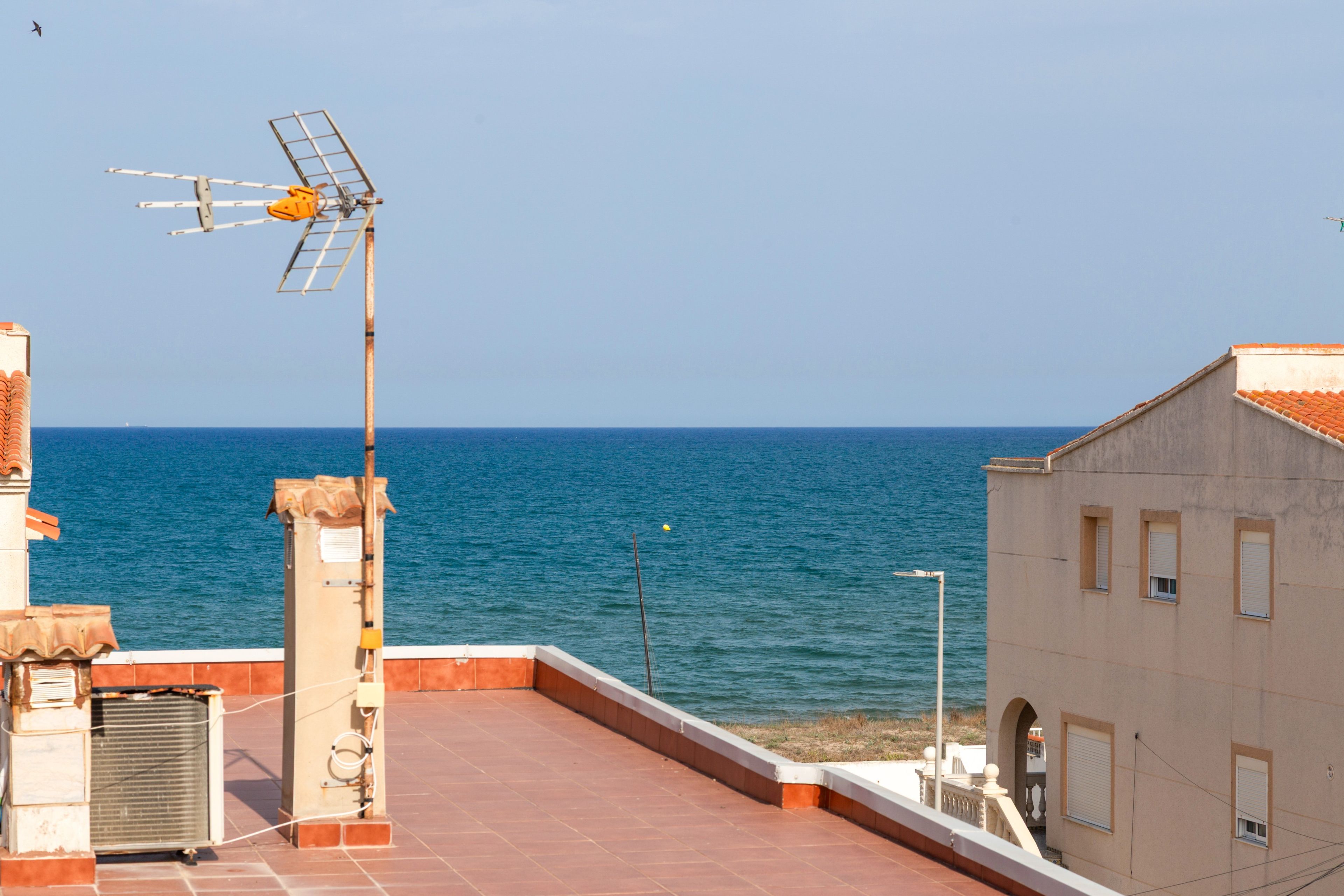 Une terrasse sur le toit offrant une vue sur la mer, une antenne parabolique et un bâtiment doté d’un toit en tuiles.