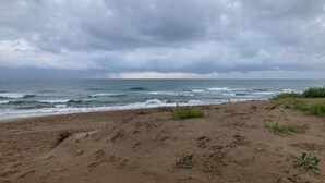 A beach with sandy terrain and ocean waves under a cloudy sky.