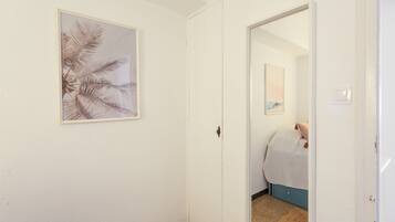 A hallway with a framed artwork on the wall, a door leading to a bedroom, and a visible bed with a blue headboard.