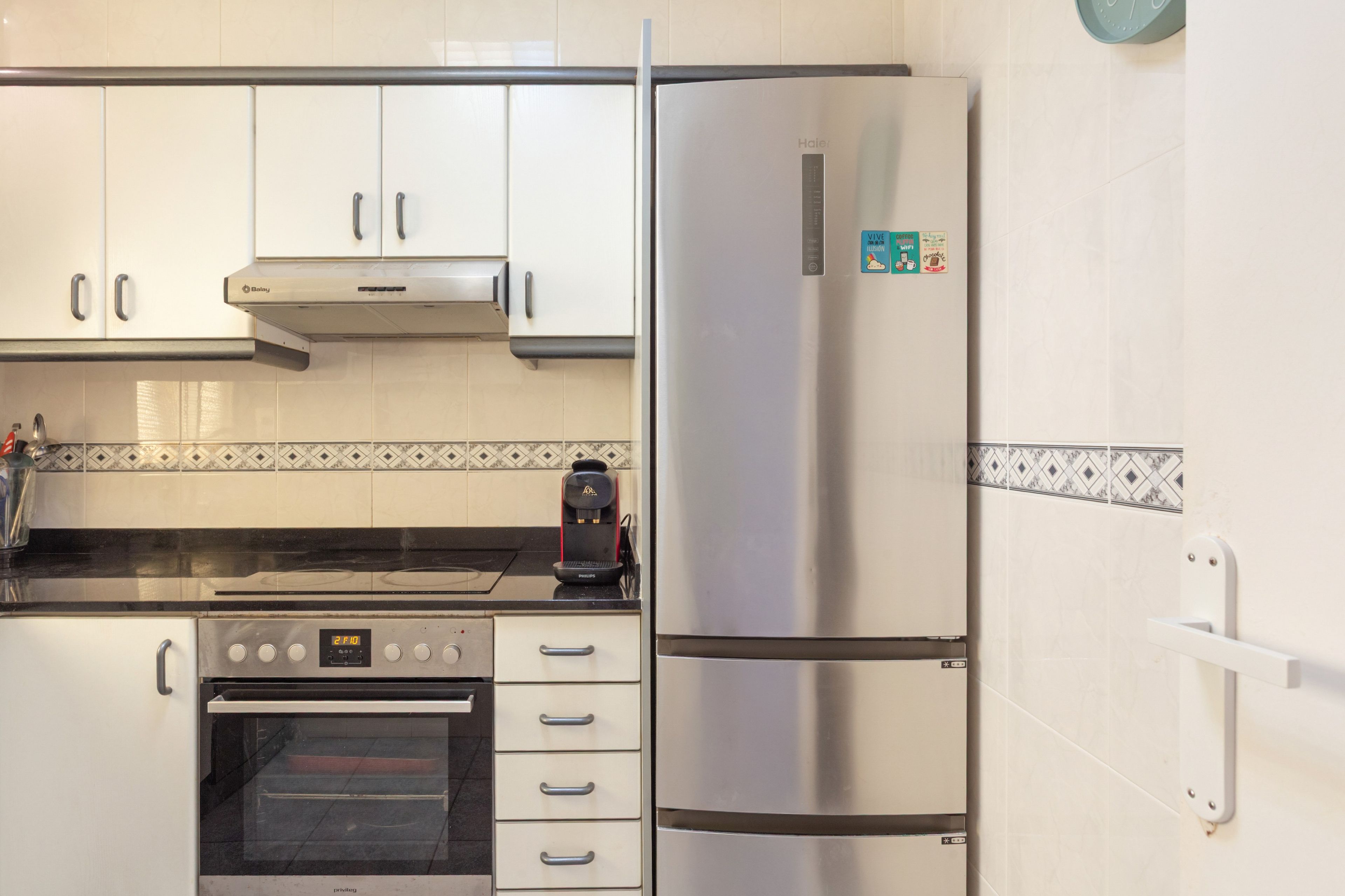 A kitchen with a stainless steel refrigerator, a built-in oven, and a coffee maker on the counter.