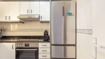 A kitchen with a stainless steel refrigerator, a built-in oven, and a coffee maker on the counter.