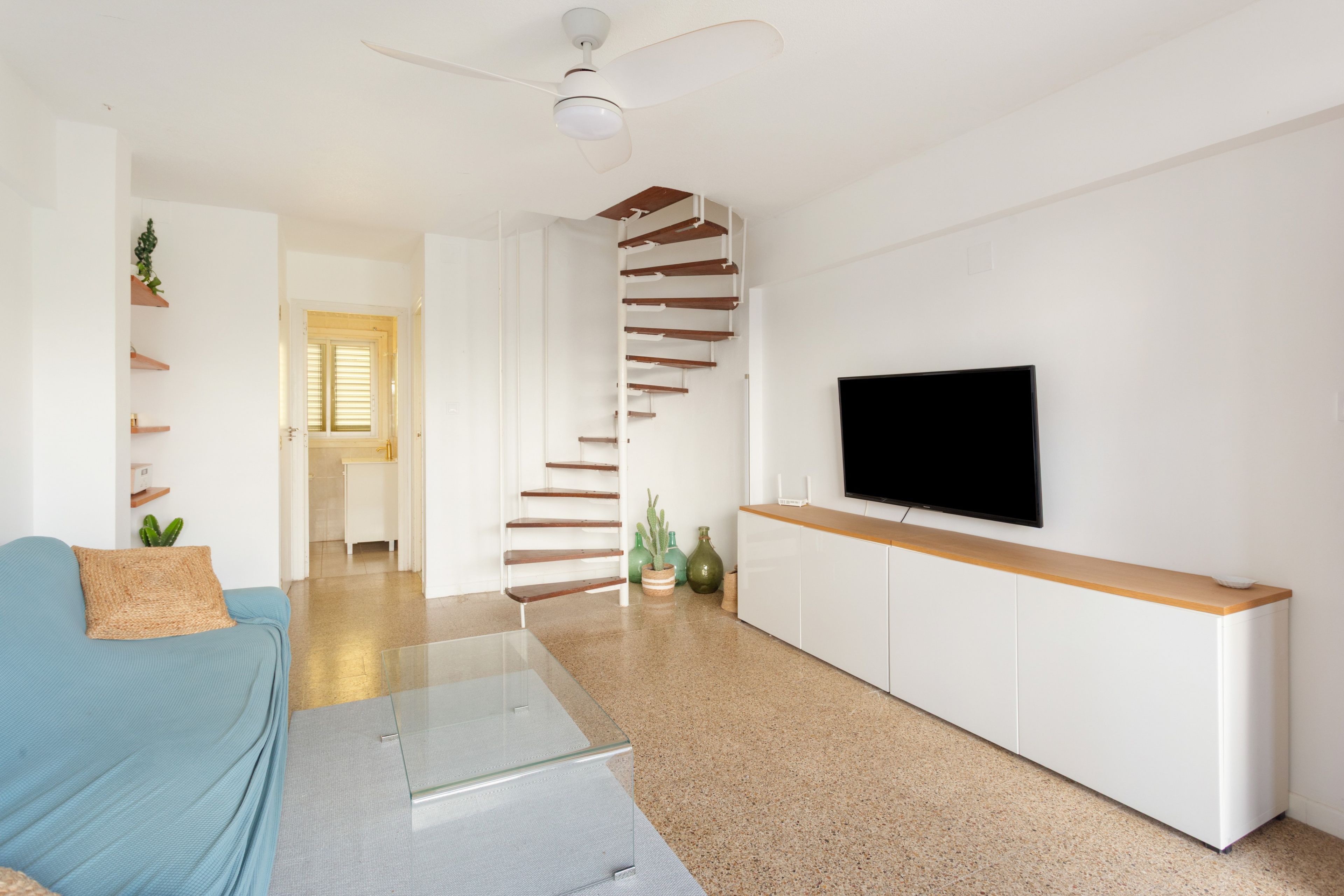A modern living room with a sofa, a TV, a staircase, and a ceiling fan.