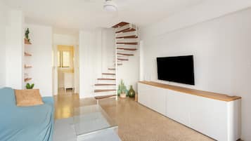 A modern living room with a sofa, a TV, a staircase, and a ceiling fan.
