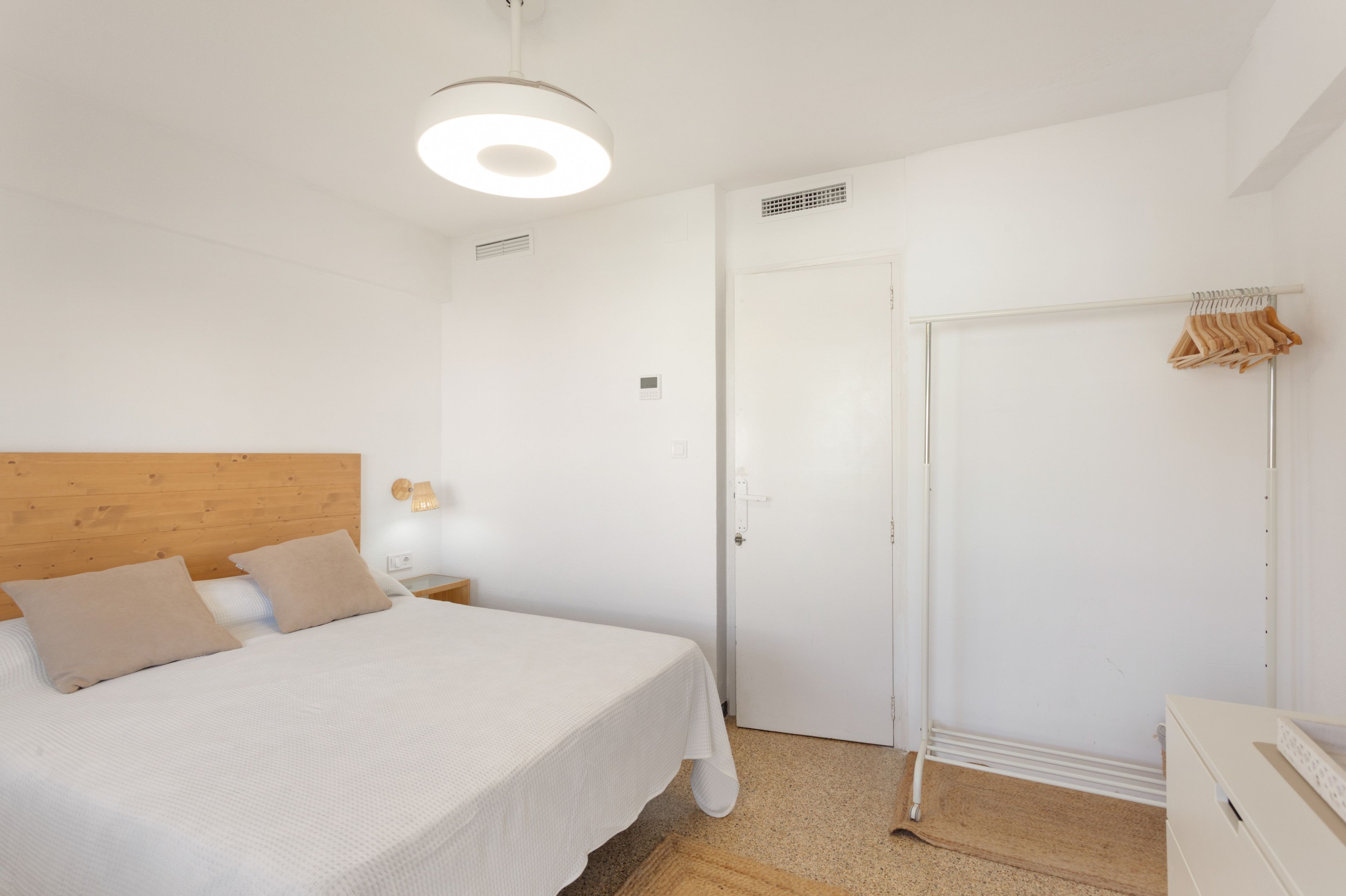 Quarto com cama, guarda-roupa, cabideiro e luminária no teto.