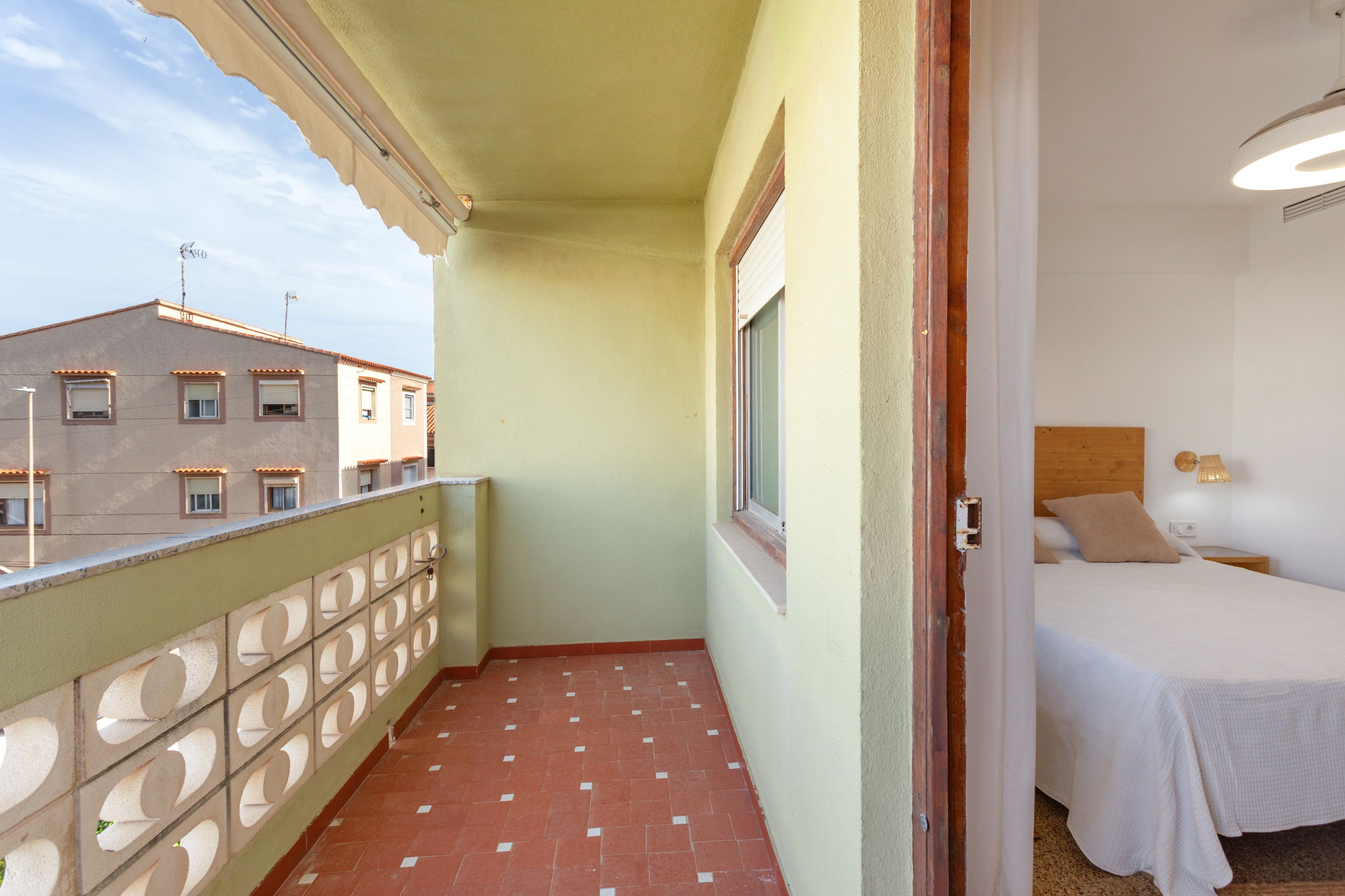 A narrow balcony with a tiled floor, a window, and a view of buildings.