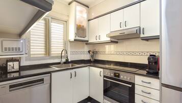 A modern kitchen with white cabinets, a black countertop, a built-in microwave, a coffee maker, and a dishwasher.