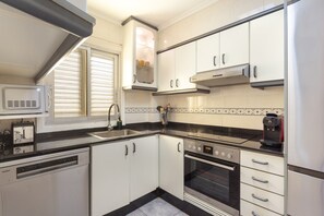 Una cocina moderna con armarios blancos, encimera negra, microondas integrado, cafetera y lavavajillas.