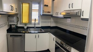 A compact kitchen with a dishwasher, stove, and a small window with blinds.