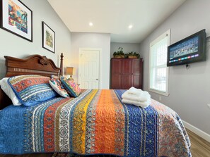 A bedroom with a large bed, a TV mounted on the wall, a wardrobe, and a door.